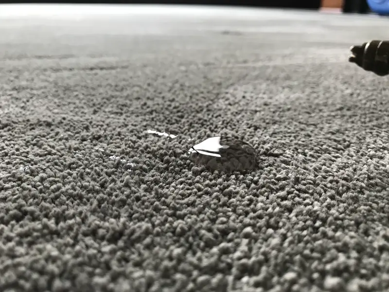 A drop of water sitting on top of a gray carpet