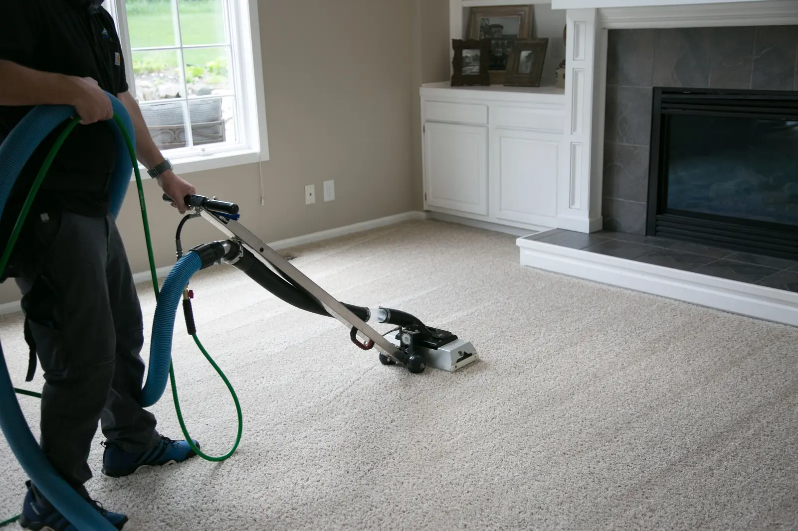 Russ cleaning a living room carpet with a wand, blue hose behind him