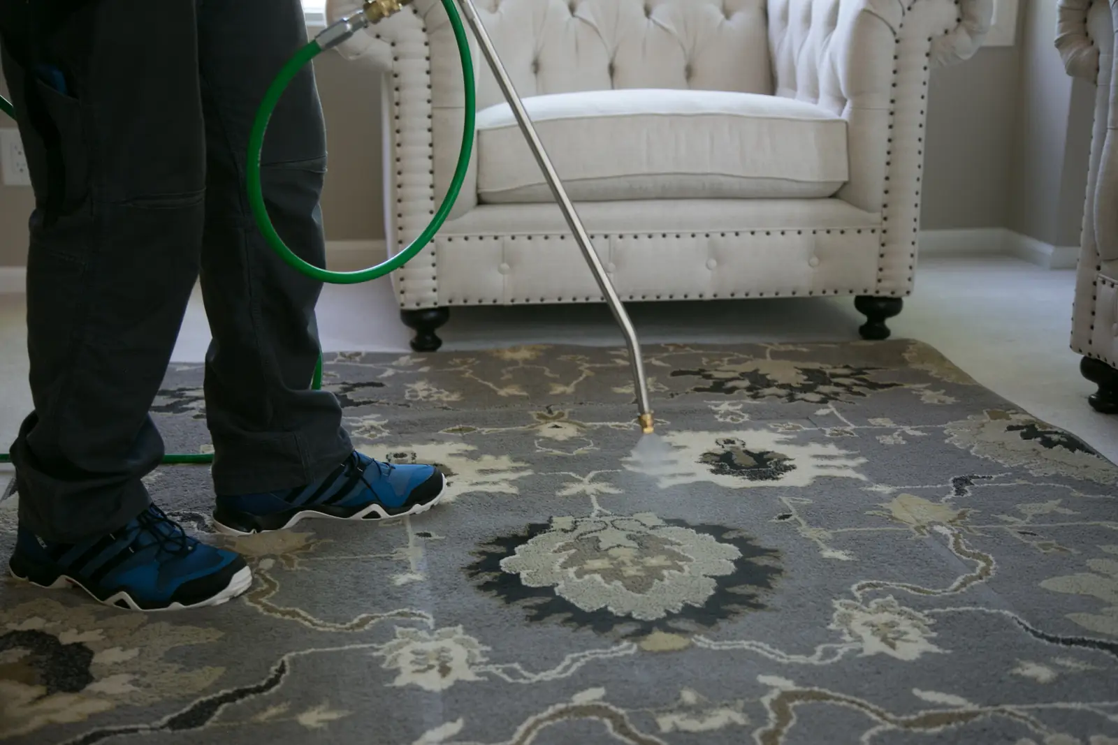 A wand cleaning a floral area rug in a living room, a white tufted chair behind