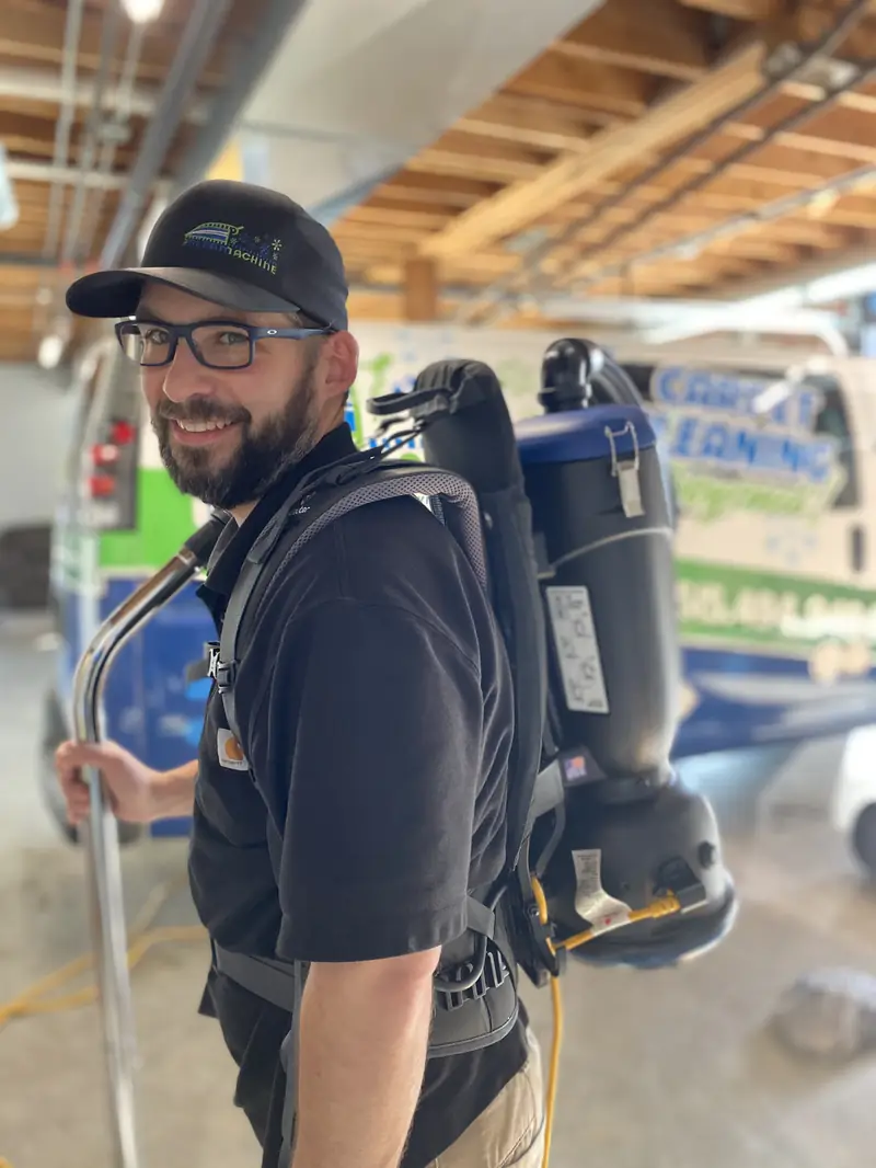 Russ wearing a backpack vacuum in the shop, the van behind him